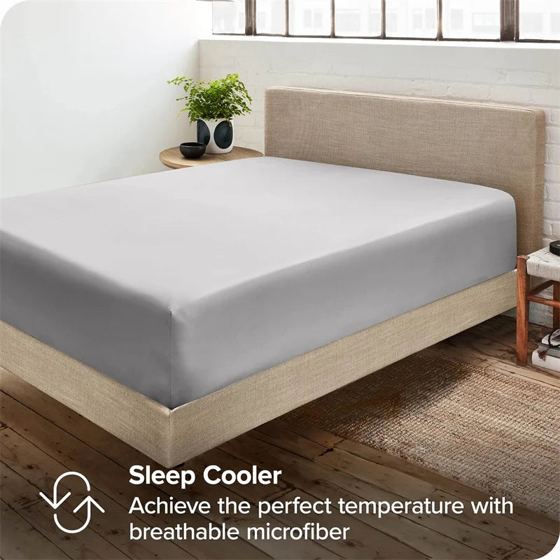 Una sábana ajustada de color gris claro sobre un marco de cama de madera con fondo de pared blanca.