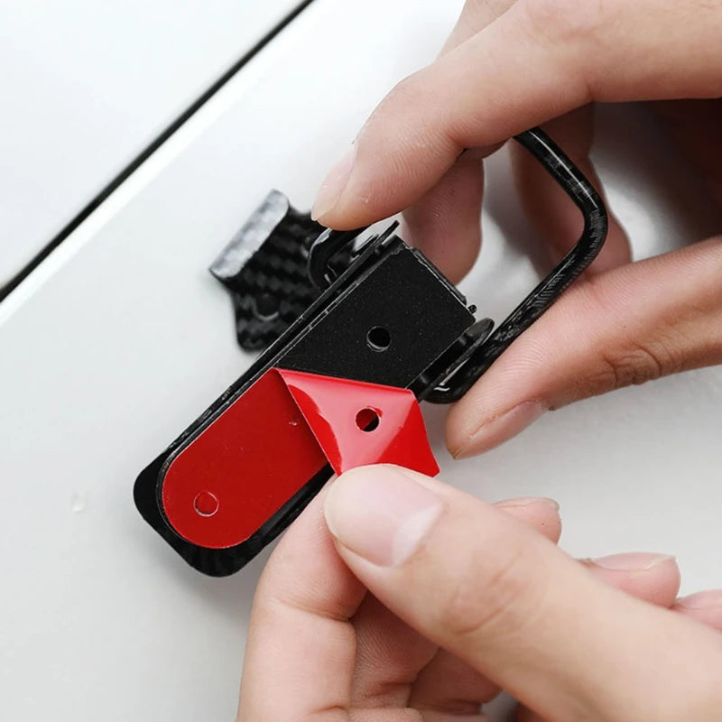 A hand is holding a black carbon fiber rear trunk locking buckle set with a red component.