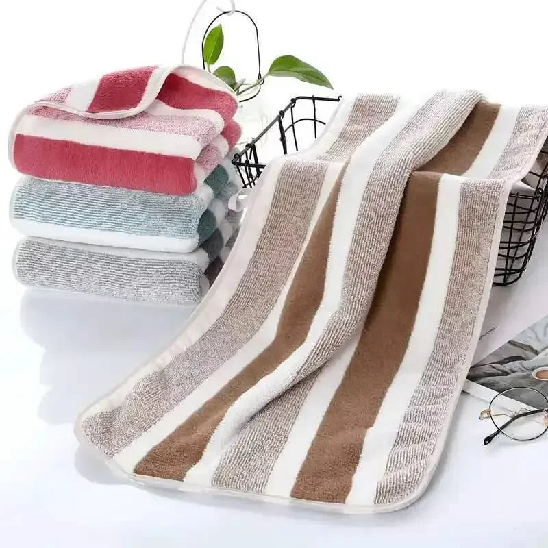 A set of striped microfiber towels in shades of pink, green, and beige are displayed on a white surface.
