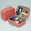 A pink faux leather portable sewing kit box with an open lid showing various needles, thread, and tools.