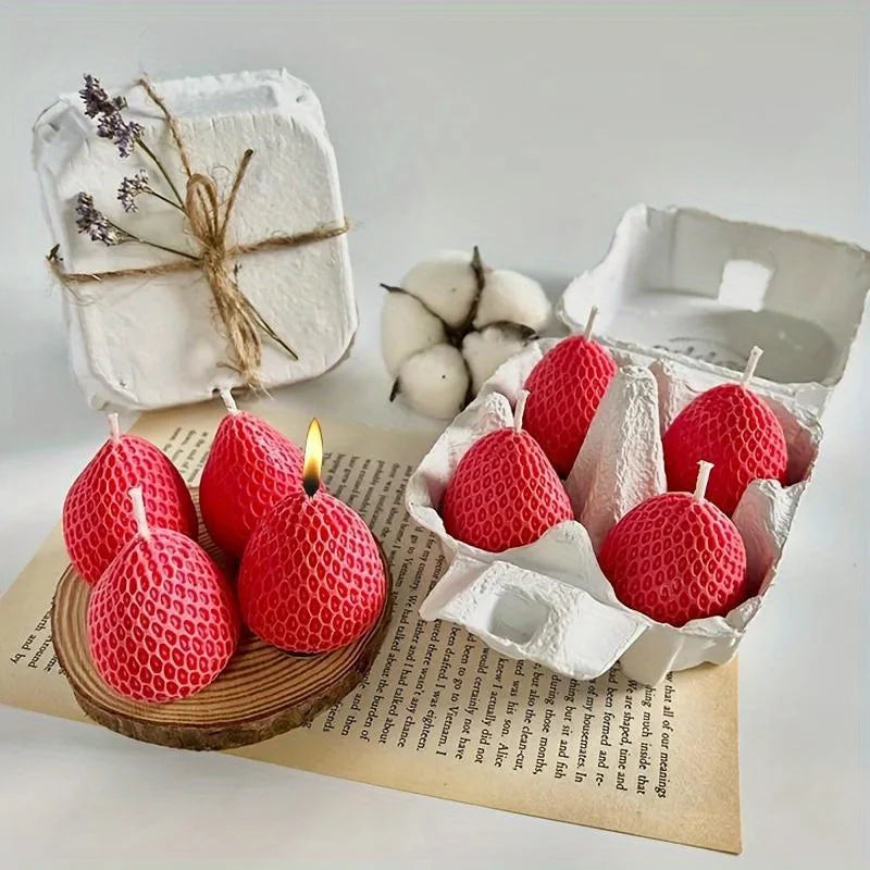 Un moule en silicone rouge en forme de fraise, exposé dans une boîte ouverte avec de la ficelle naturelle et des morceaux de 