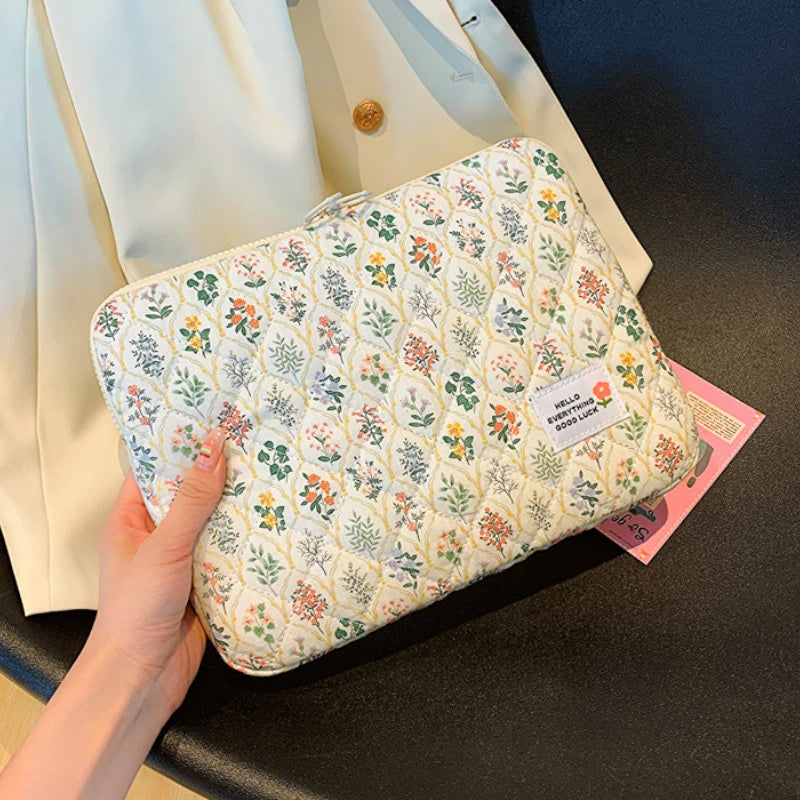 A floral printed laptop sleeve with a zipper closure is being held by a hand, set against a dark surface.