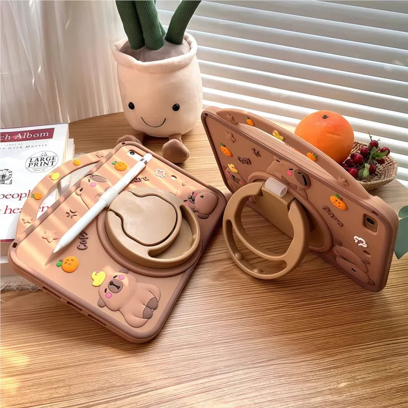 A light brown silicone case featuring a cute cartoon capybara design for an iPad, placed next to a potted plant.