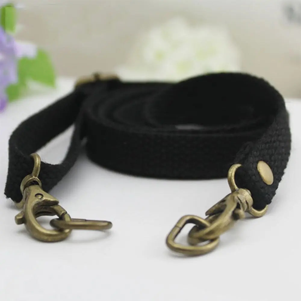 Black adjustable canvas shoulder strap with brass hardware lying on a white surface.