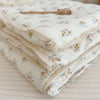 A stack of white floral muslin baby blankets with delicate lace trim and a wooden thimble.