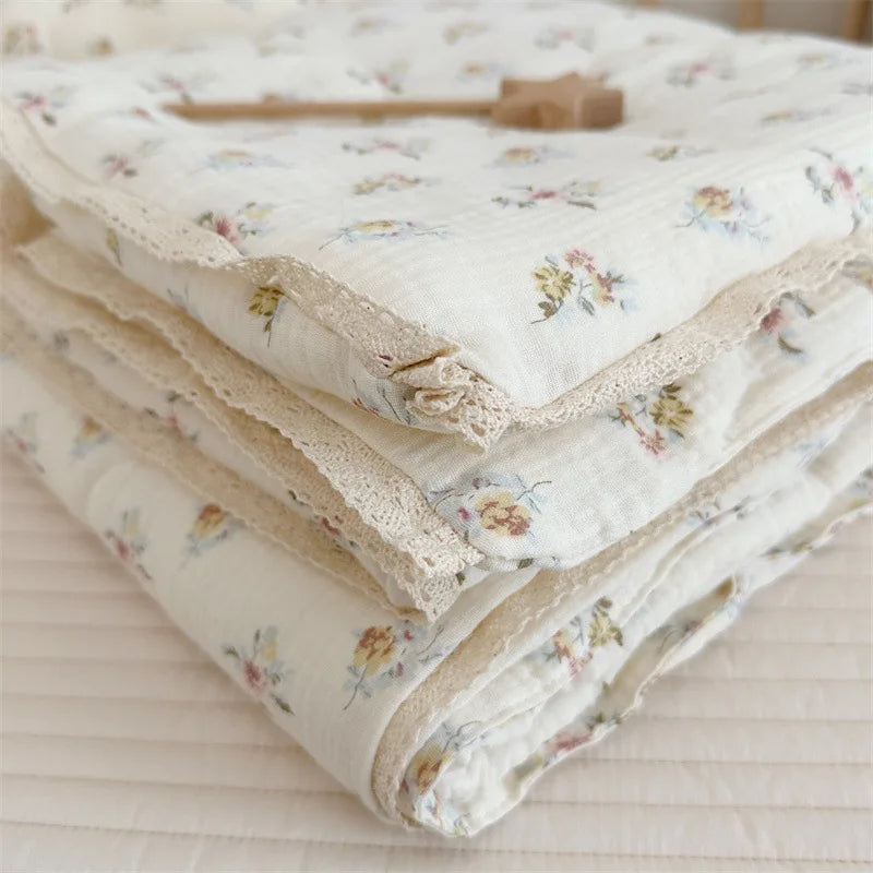 A stack of white floral muslin baby blankets with delicate lace trim and a wooden thimble.