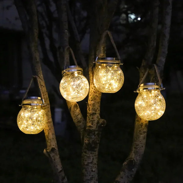 Tira de farolillos solares de vidrio craquelado brillando en ramas de árboles por la noche.