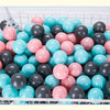 A white basket filled with a large pack of colorful plastic ball pit balls in shades of pink, blue, and gray.