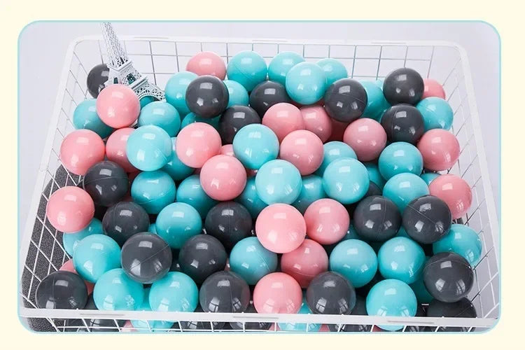 A white basket filled with a large pack of colorful plastic ball pit balls in shades of pink, blue, and gray.