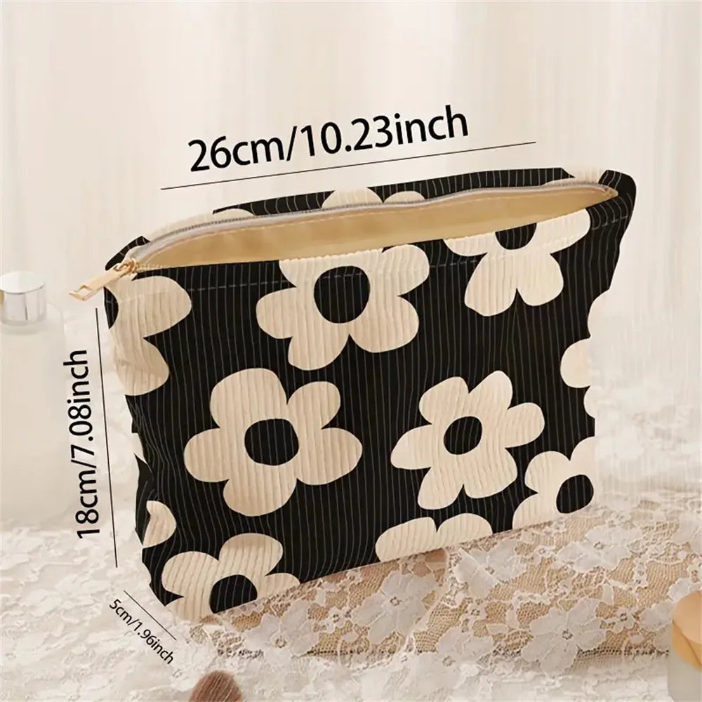 A black and cream floral corduroy makeup bag with a zipper is displayed on a lace surface.