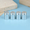 A set of four silver bullet shell tire valve stem caps resting on a light blue surface next to a wooden block.