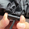 A hand is holding a black heavy-duty waterproof charcoal grill cover, showing the textured fabric and a strap.