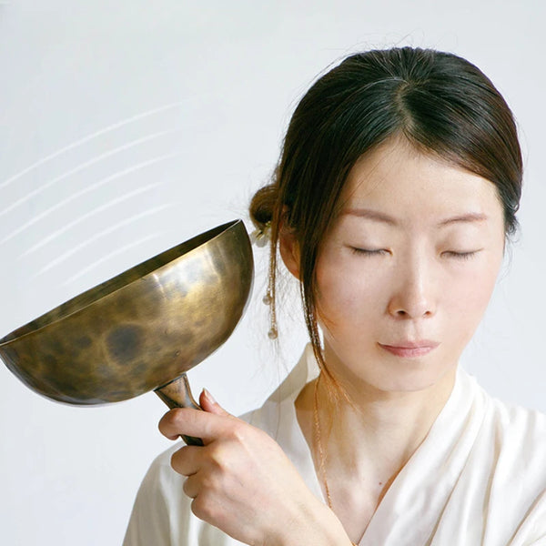 A woman is gently striking a handcrafted Tibetan singing bowl with a wooden mallet.