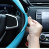 A hand is adjusting a light blue silicone steering wheel cover on a black car steering wheel.