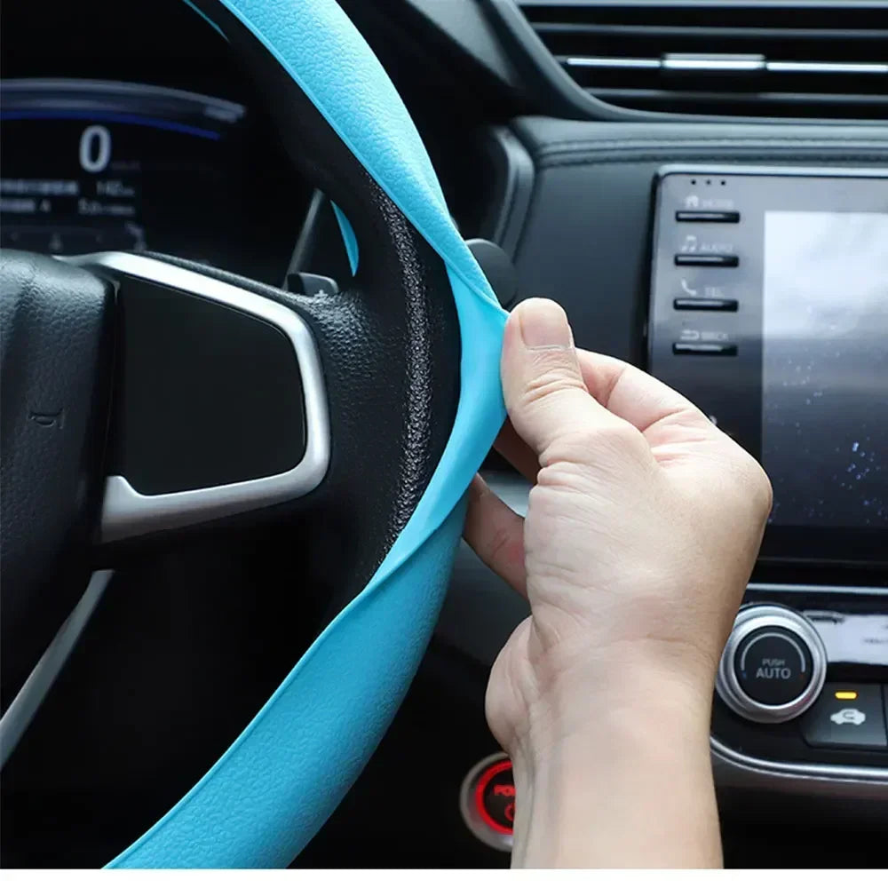 A hand is adjusting a light blue silicone steering wheel cover on a black car steering wheel.