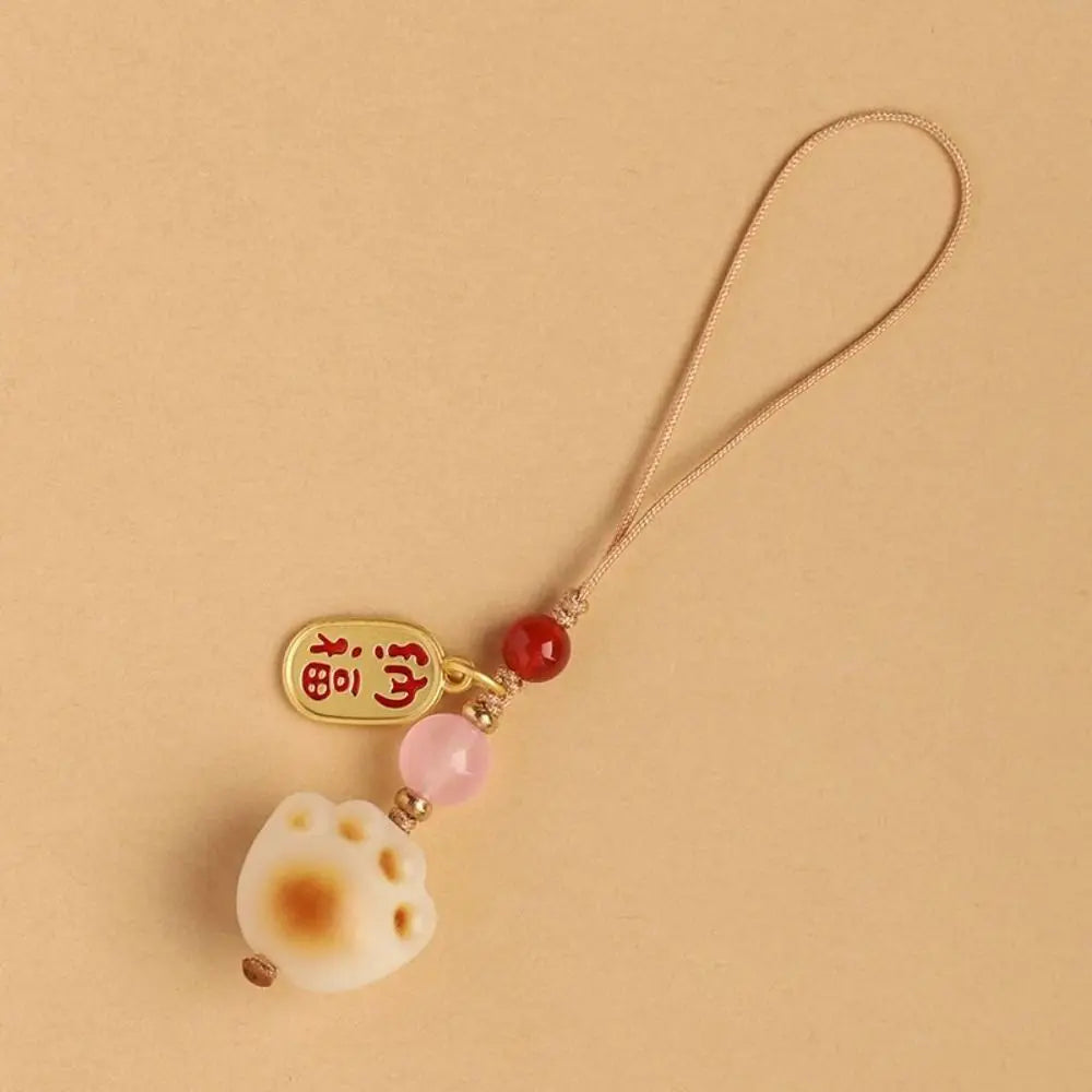A gold-colored keychain pendant featuring a charm of a white dog paw print and pink beads on a thin cord.