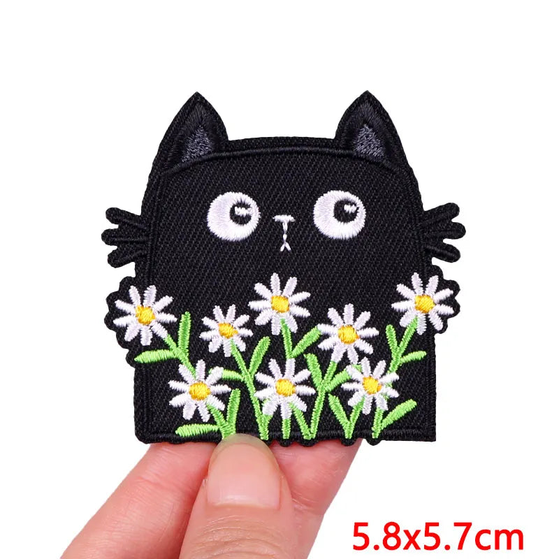 Black cat embroidery patch with white floral accents on a finger