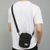 A person wearing a white t-shirt is shown from the back, carrying a black mini crossbody phone bag with an adjustable strap.