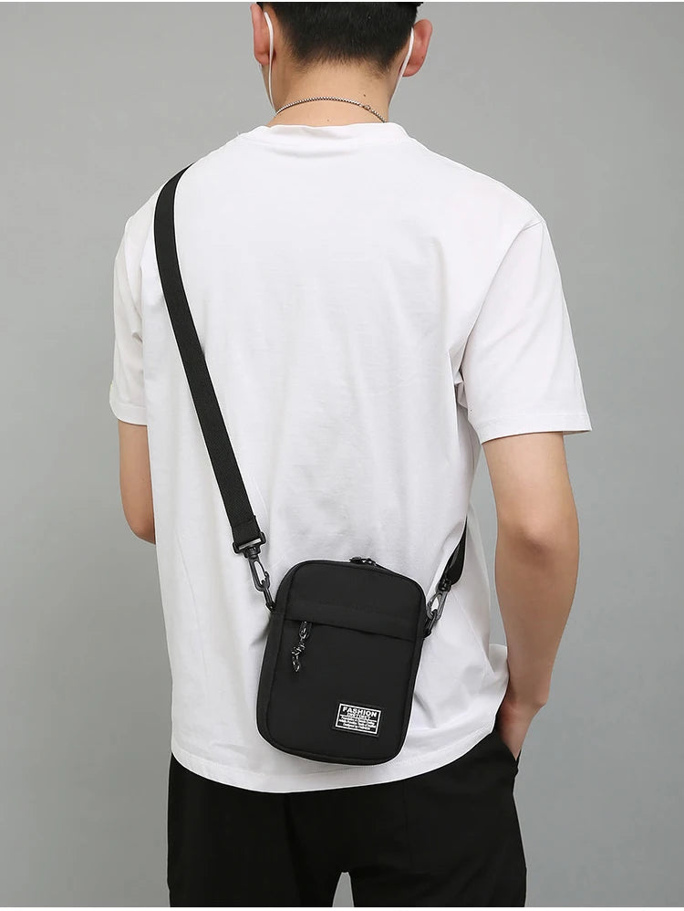A person wearing a white t-shirt is shown from the back, carrying a black mini crossbody phone bag with an adjustable strap.