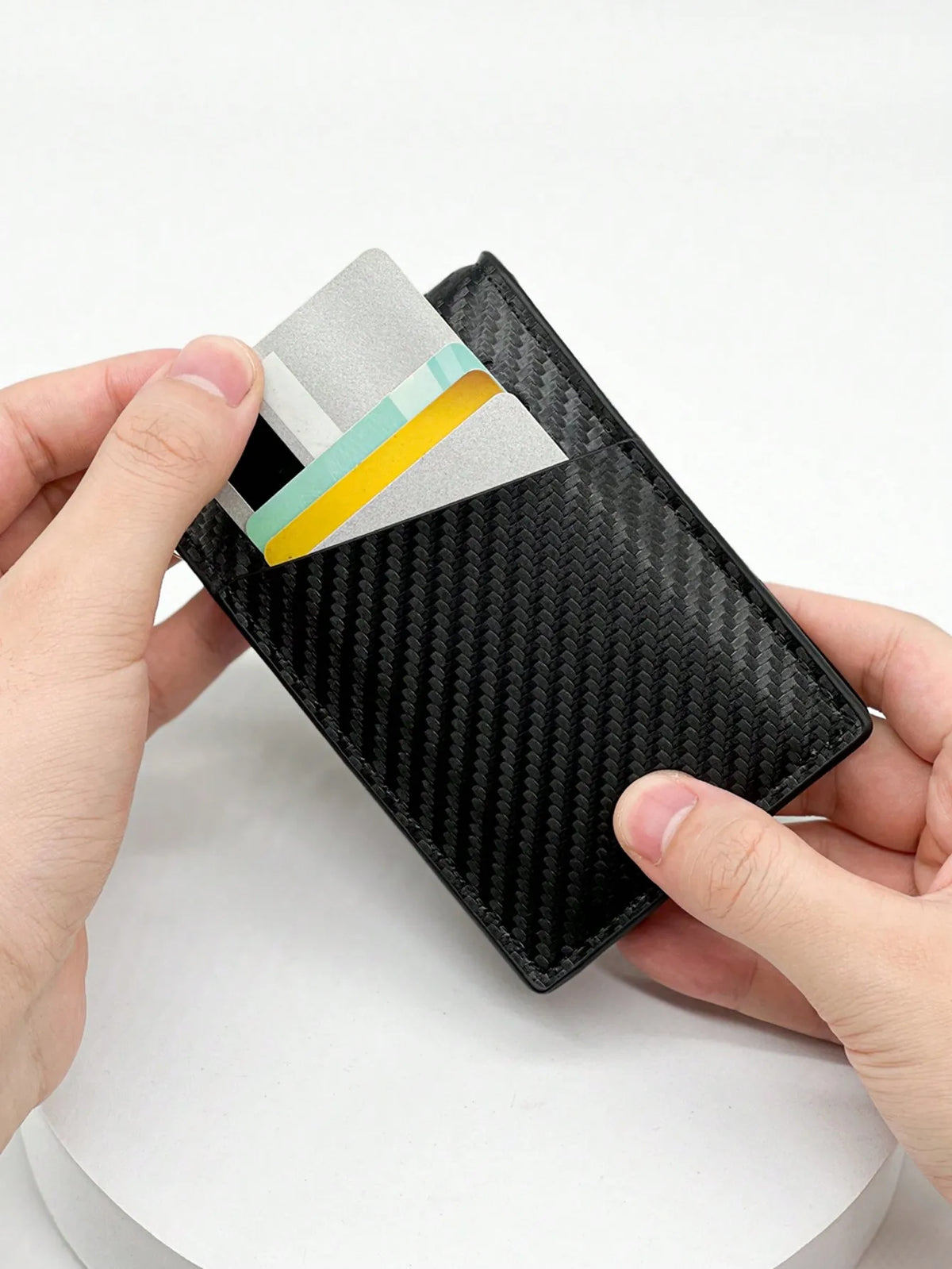 Eine Hand hält eine schwarze Kohlefaser-Kartenträger-Geldbörse mit einer silber-grünen Karte eingelegt.