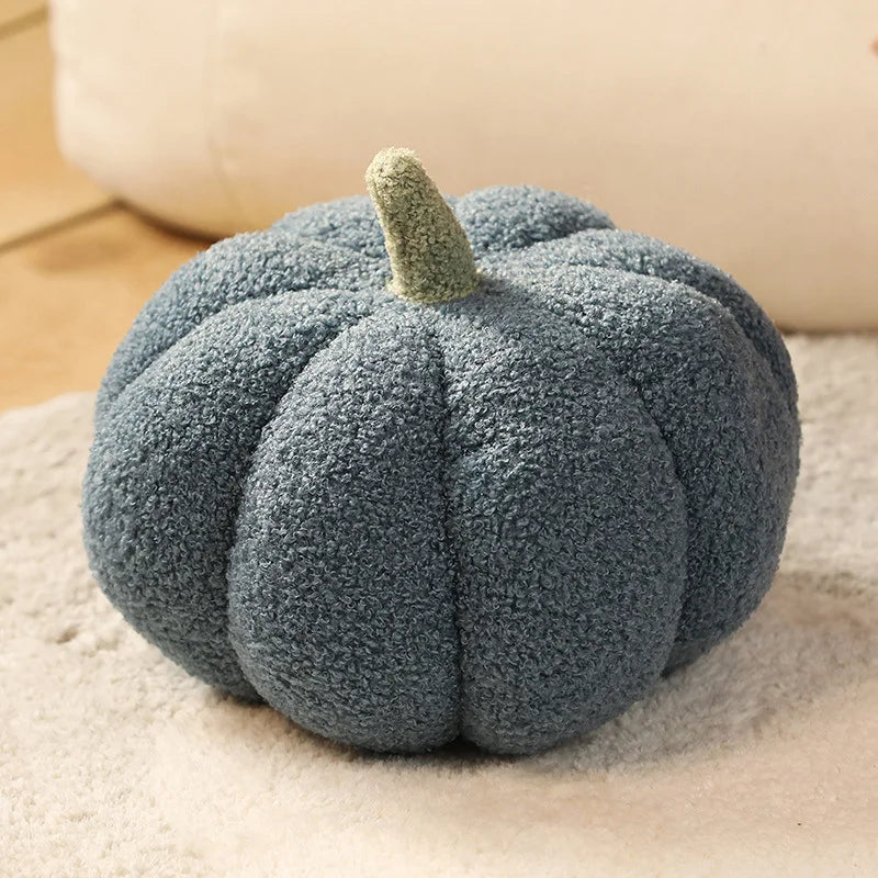 A round, fuzzy gray pumpkin plush cushion with a green stem resting on a light surface.