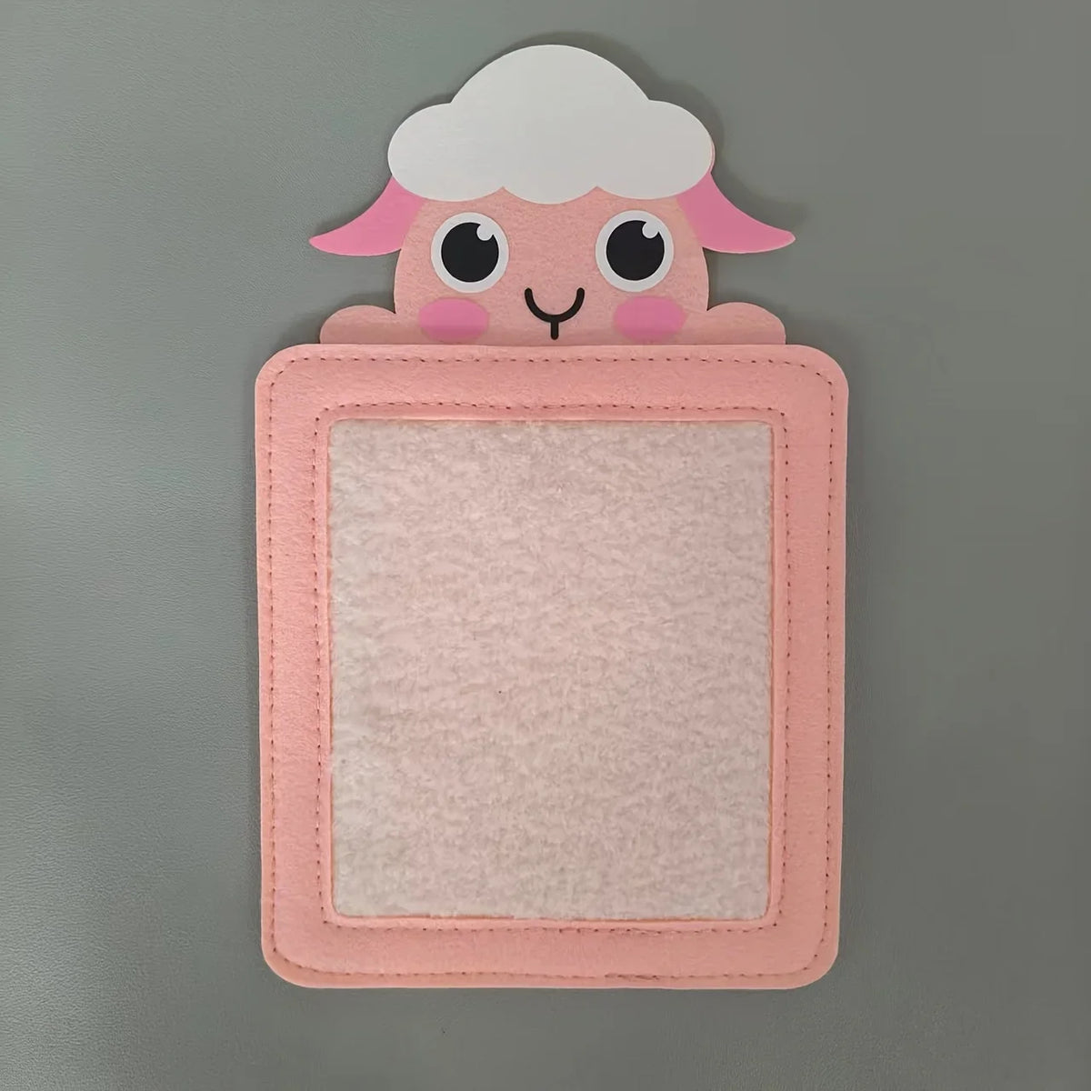 A pink felt board featuring a cute white fluffy animal face with pink ears and eyes.