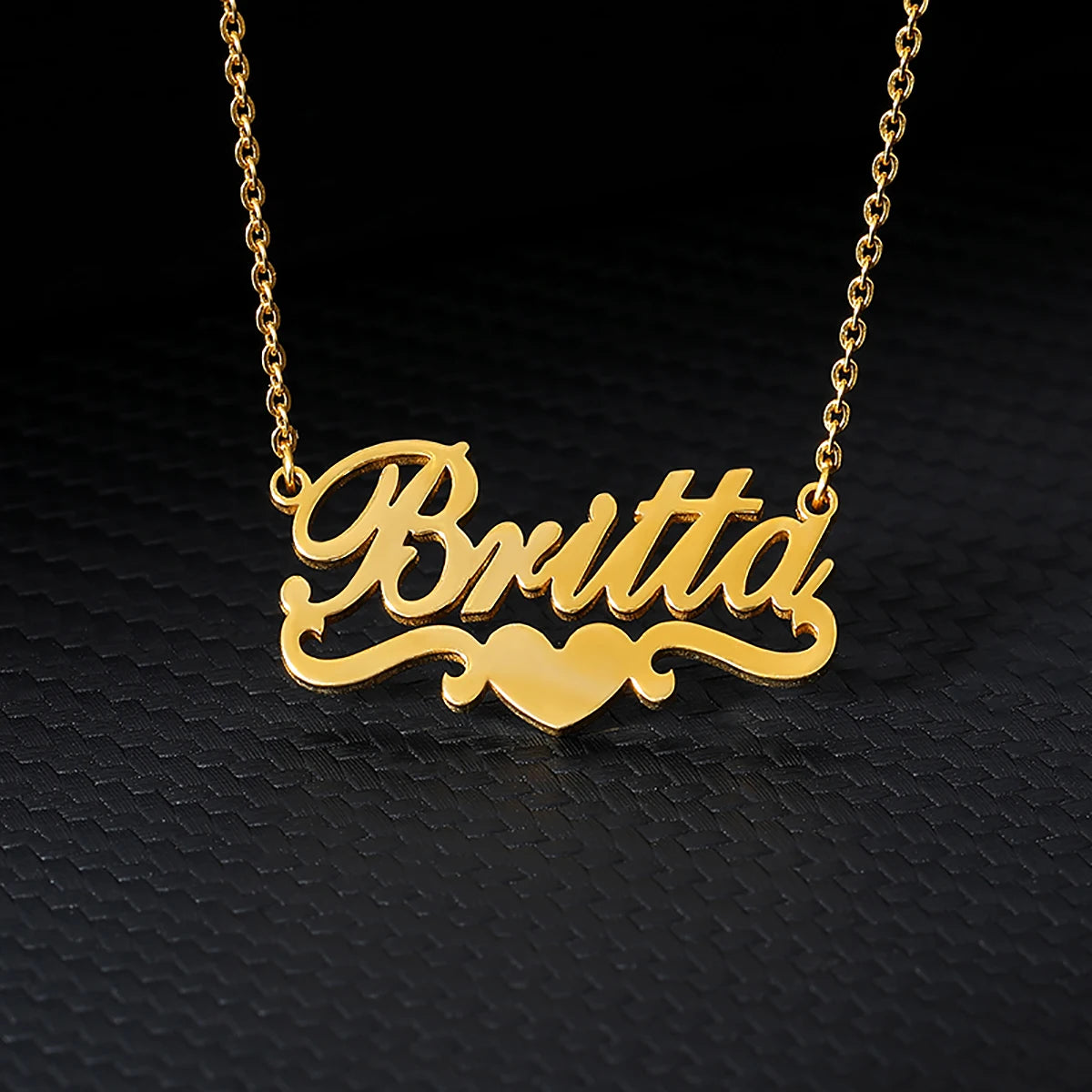 Collier nom en acier inoxydable couleur or, épelant Britta sur fond noir.
