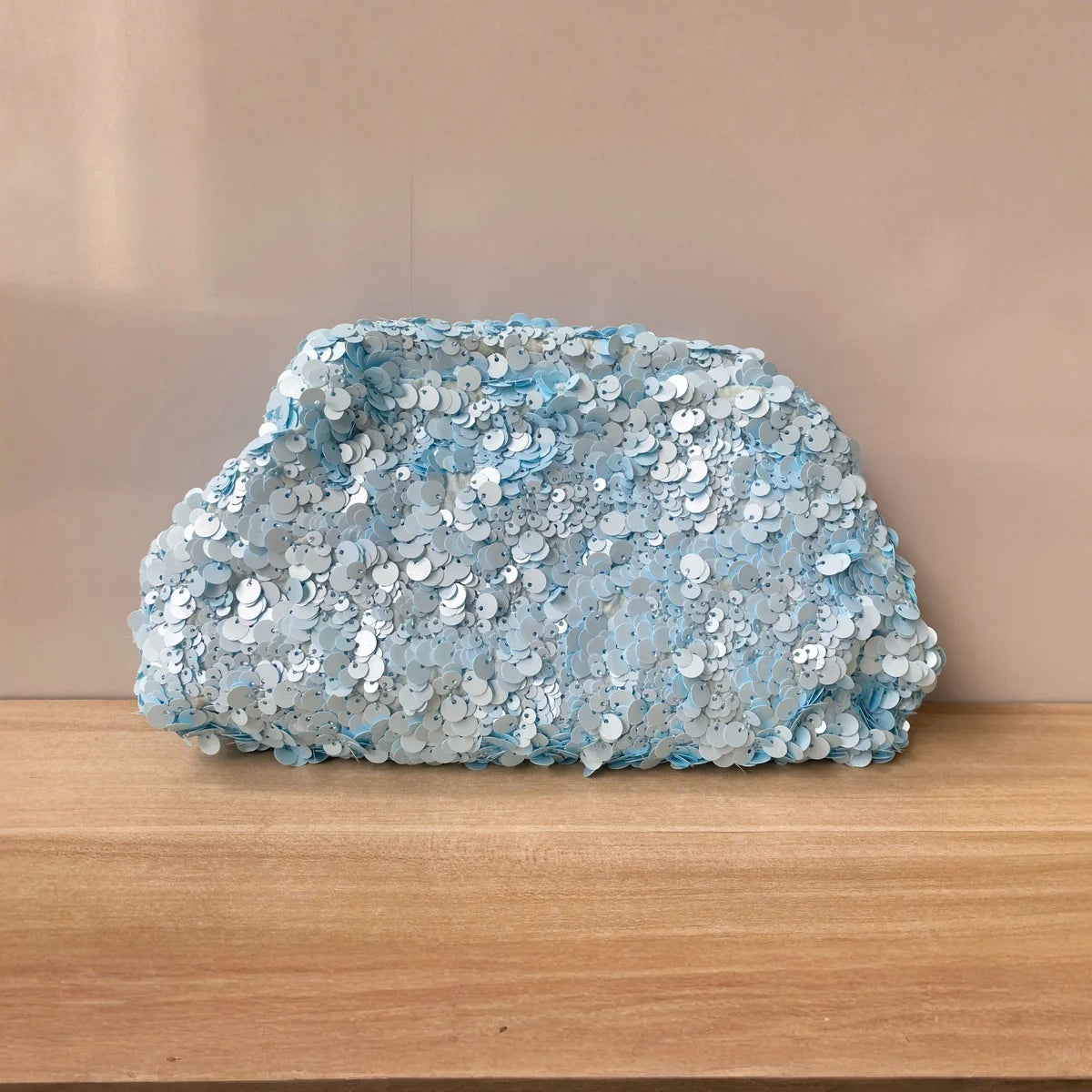 A light blue sequin beaded chain shoulder clutch bag resting on a wooden surface.