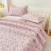 Pink floral quilted bedspread with a white border and matching pillows on a bed.