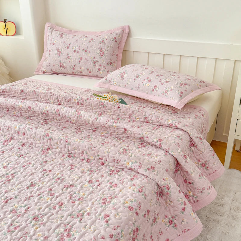 Pink floral quilted bedspread with a white border and matching pillows on a bed.