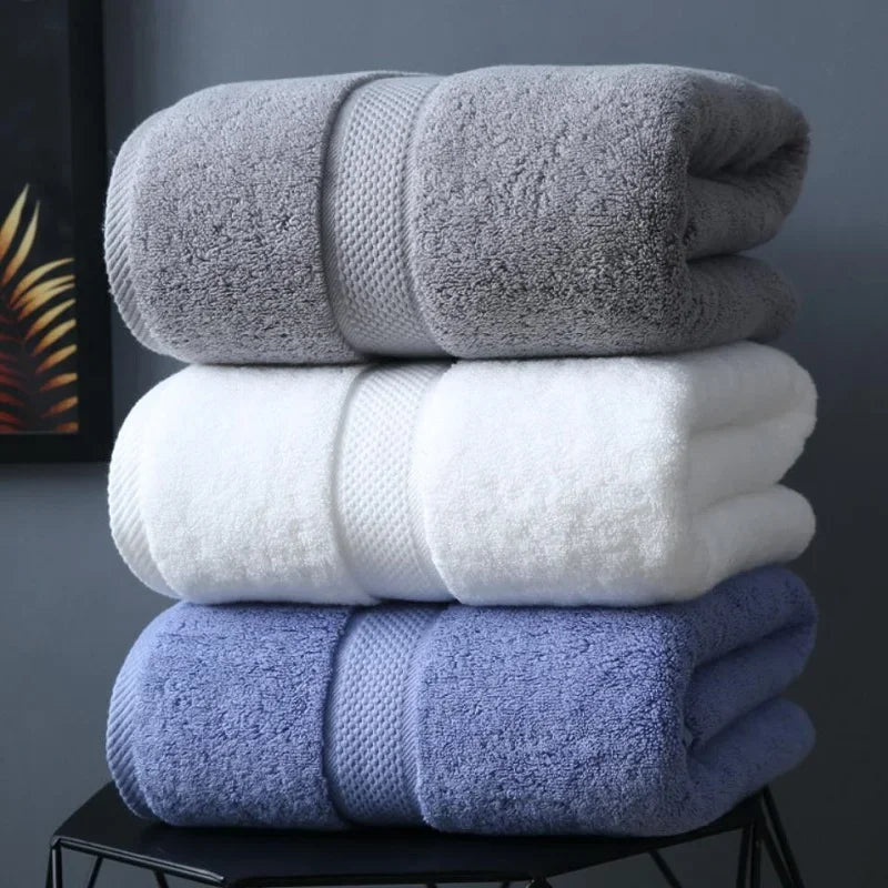 A stack of three bath towels in gray, white, and blue folded on a black surface.