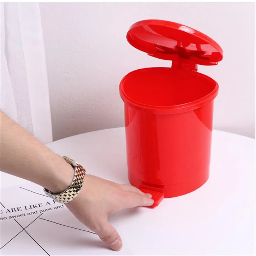 A hand is holding a bright red mini strawberry trash can with a pop-up lid on a white surface.