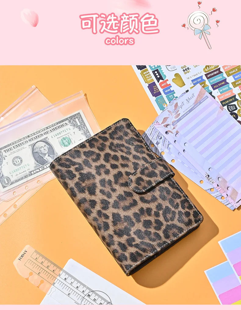 Leopardmuster-Budgetplaner-Notizbuch neben US-Dollar und Lineal auf orangem Hintergrund.