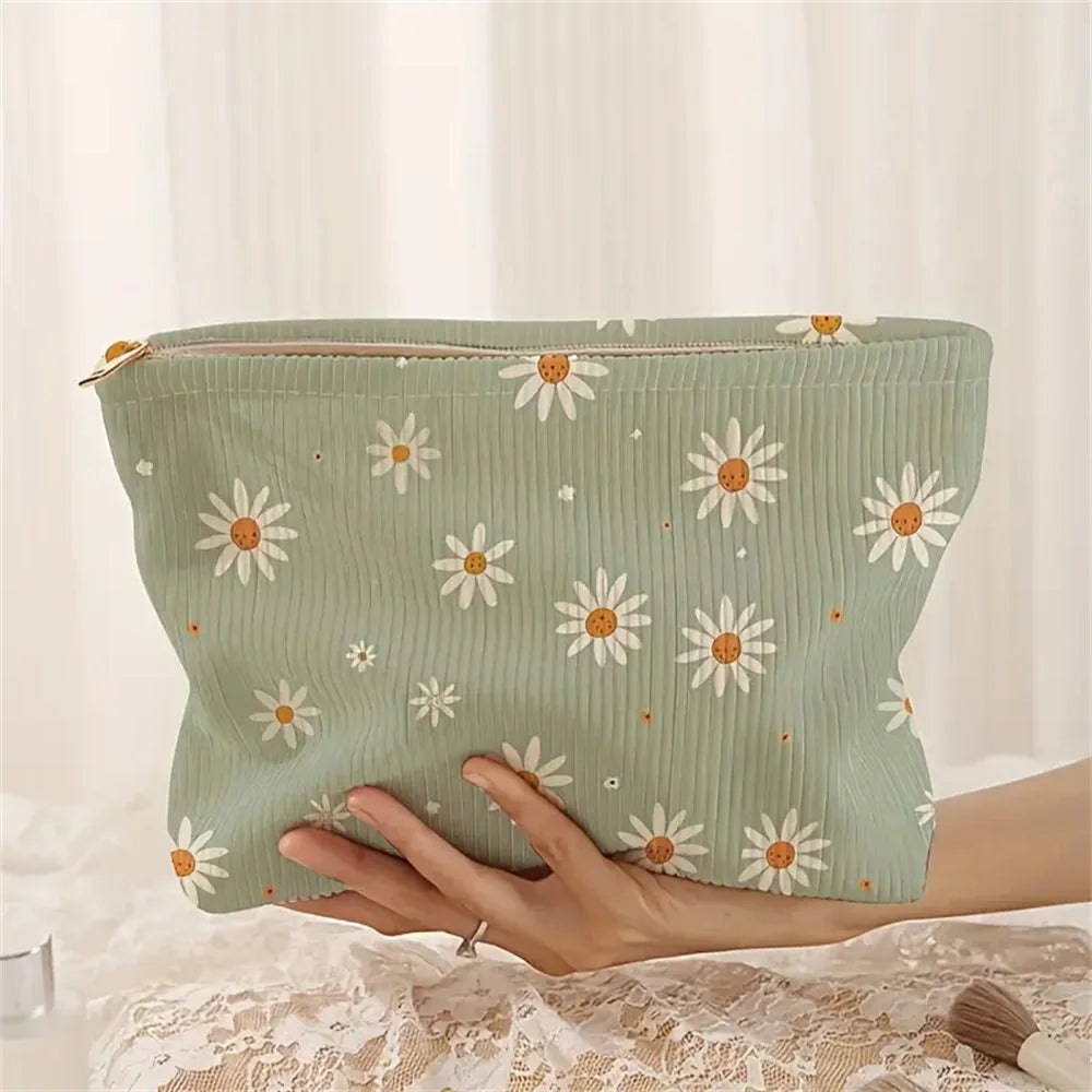 A hand holds a light green floral corduroy makeup bag with a zipper on a white lace surface.