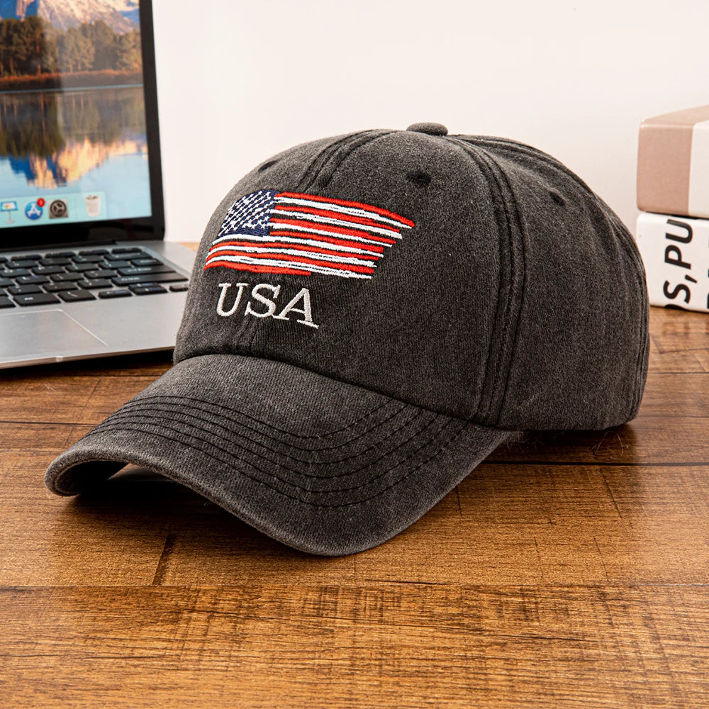 A gray baseball cap embroidered with the American flag and the letters USA resting on a wooden surface.