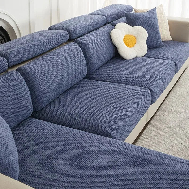 A blue jacquard elastic sofa slipcover with a white flower cushion on a light-colored sofa.
