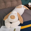A white dog plush pillow with tan ears resting on a gray surface.