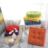 A collection of thick corduroy floor cushions in various shades of green, yellow, and blue are displayed on a white table.