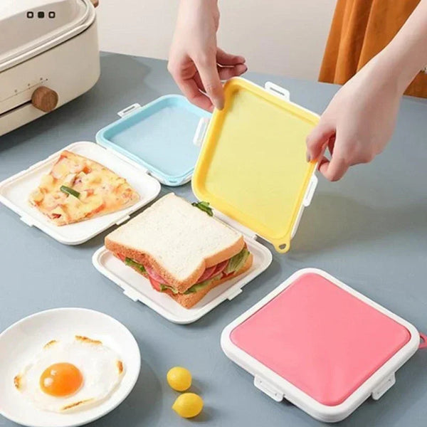 Hands are placing a yellow silicone sandwich crisper into a white lunch box next to a plate of food.
