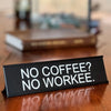 A black desk sign with white text that reads NO COFFEE NO WORKEE and NO MONKEY on a wooden surface.