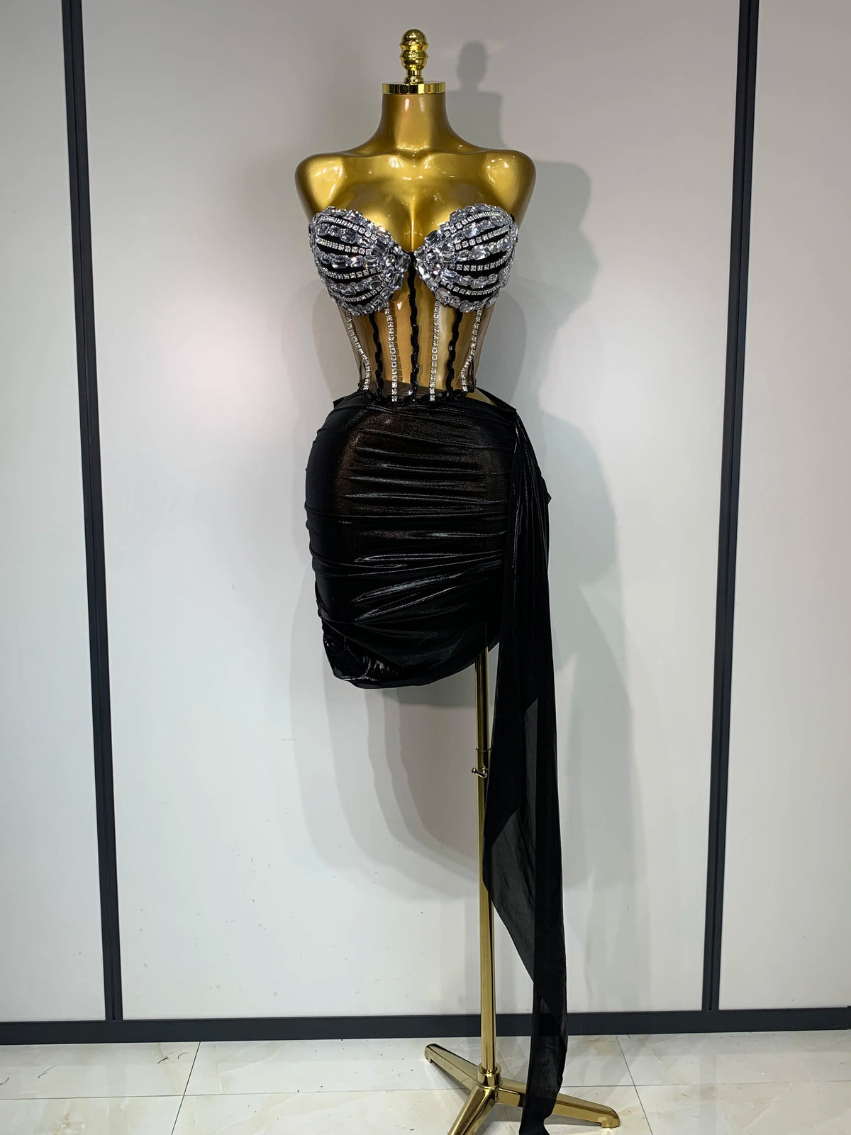 A mannequin displays a sparkly two-piece party outfit featuring a sheer top and a black draped skirt.