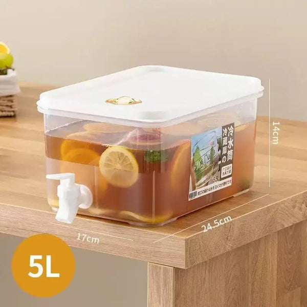 Dispensa de bebidas de plástico transparente con tapa blanca y caño, llena de líquido ámbar, sobre una superficie de madera.