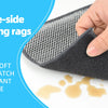A hand is holding a dark gray double-sided washing rag made of microfiber and mesh fabric, with some liquid spilled on the su