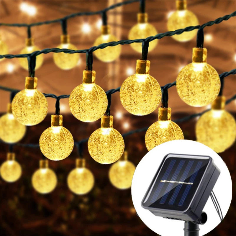 String lights featuring yellow crystal ball bulbs hanging outdoors with a solar panel visible below