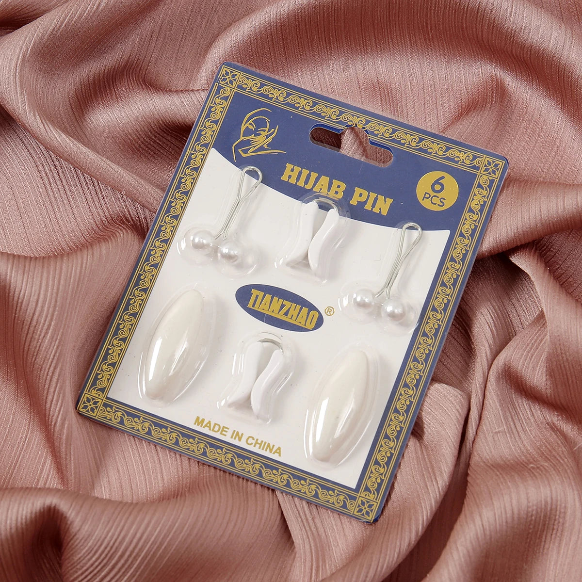 A package containing eight white pearl-style pins for hijab and scarf decoration, displayed on pink fabric.