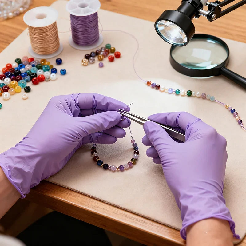 Hands in purple nitrile gloves are stringing beads onto a string under a magnifying glass.