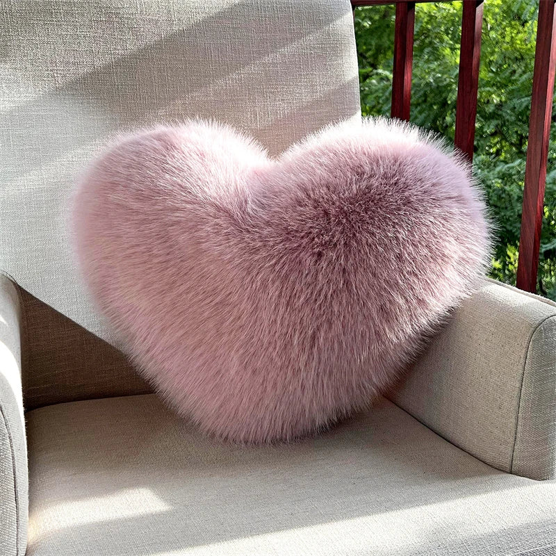 A fluffy pink heart-shaped throw pillow resting on a light-colored sofa.