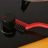 A black kitchen cleaning brush and scraper tool resting on a dark surface with a wooden edge.