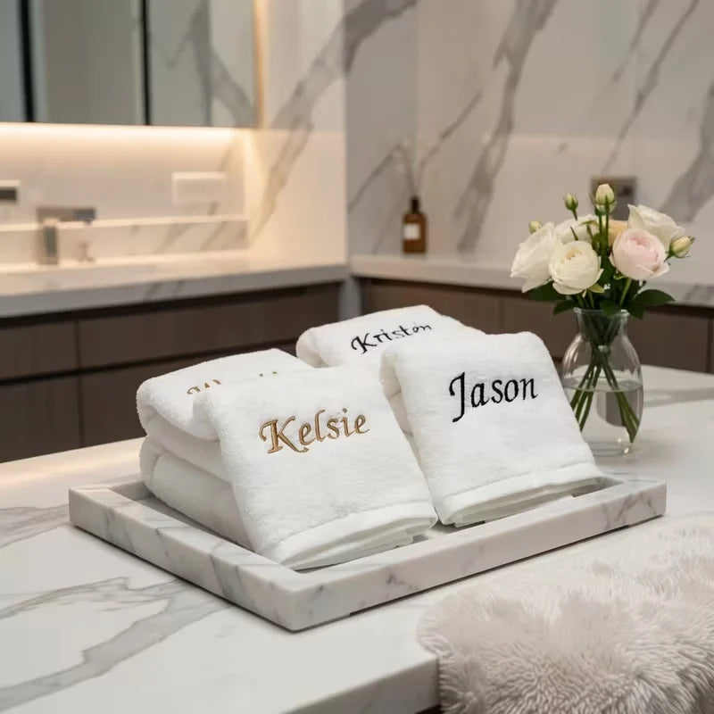 A stack of white personalized organic cotton face towels with gold lettering displayed on a marble tray.
