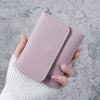 A hand holds a light mauve slim triple-fold PU leather wallet against a gray textured background.